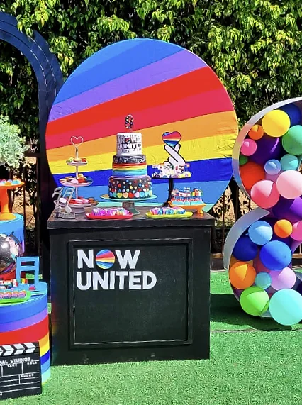 Mesa de bolo com painel de arco-íris e decoração colorida montada para uma festa na Nicolândia